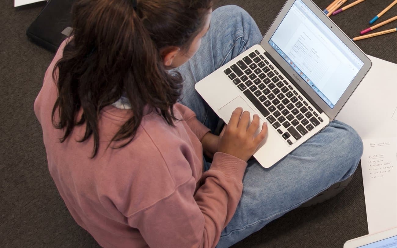 A student working on a laptop surrounded by notes and devices